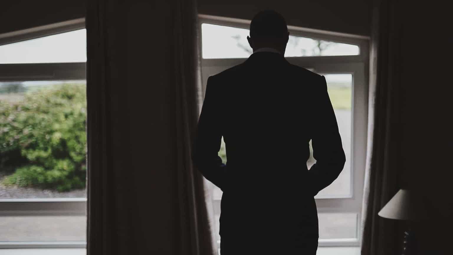 Groom is putting suit and looking outside widow.