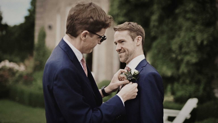 Best man is tiding buttonhole at groom shoulder