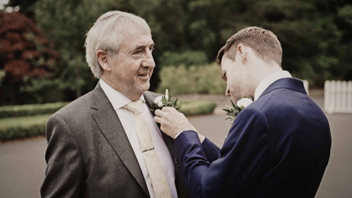 Groom attaching flower to Dad Shoulder