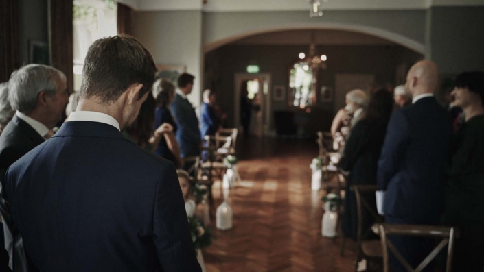Groom looking at door where bride is showing with dad.